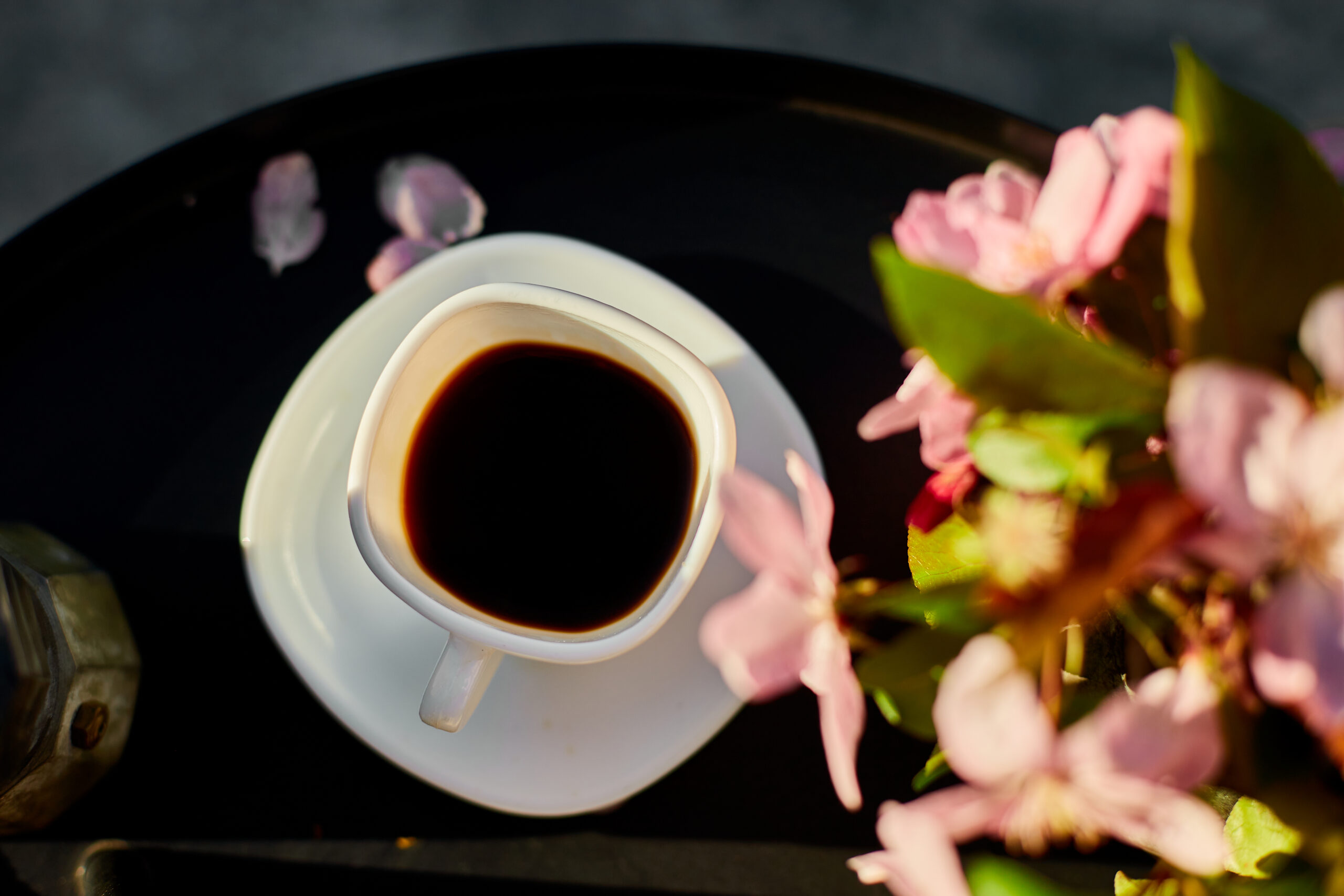 Top view Cup of coffee flowers and notebook on the small black table on terrace at home in a sunny day, outdoor workspace, summer relaxation, coffee break, representing the healthiest coffee