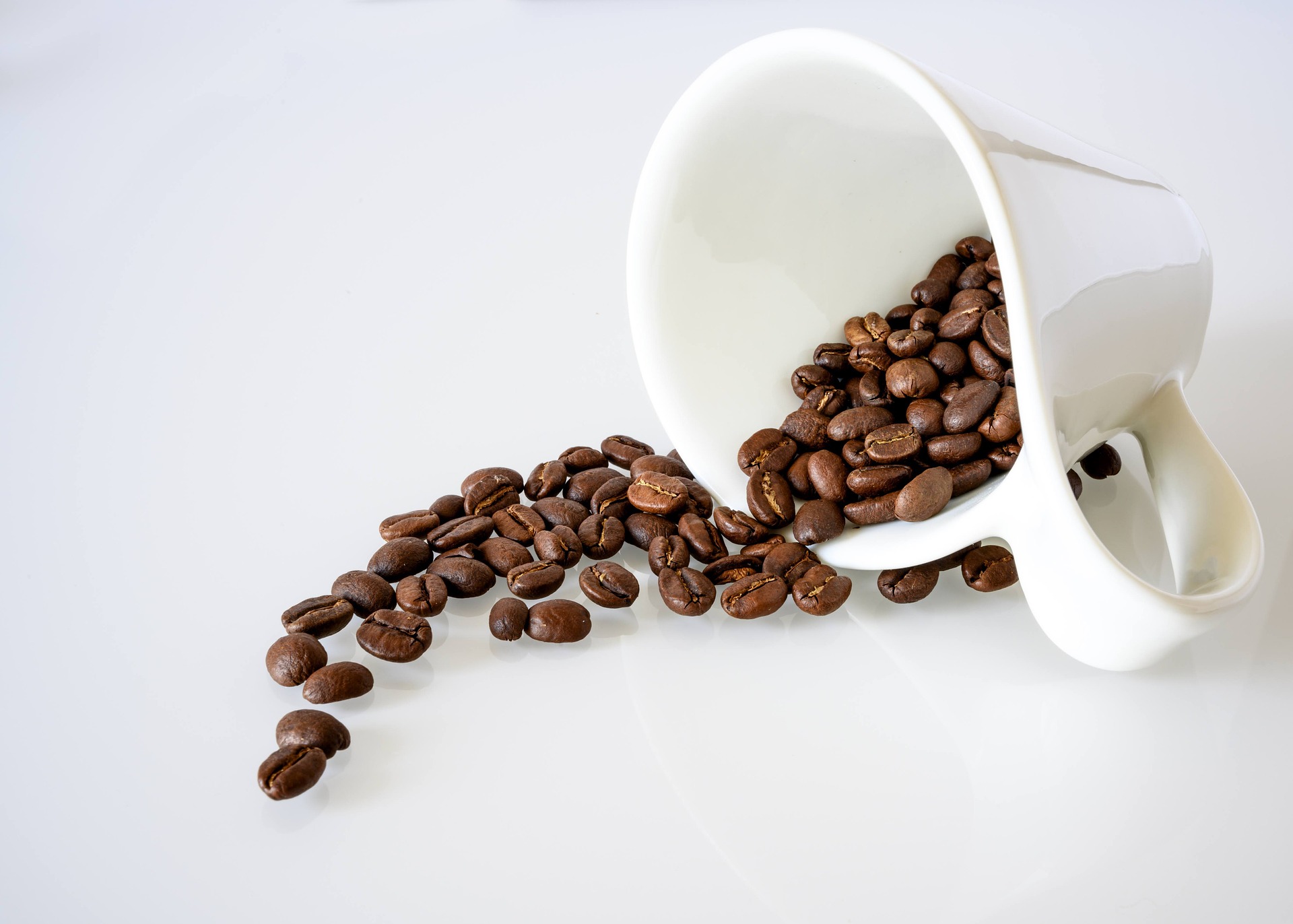 White cup spilling roasted beans on clean background